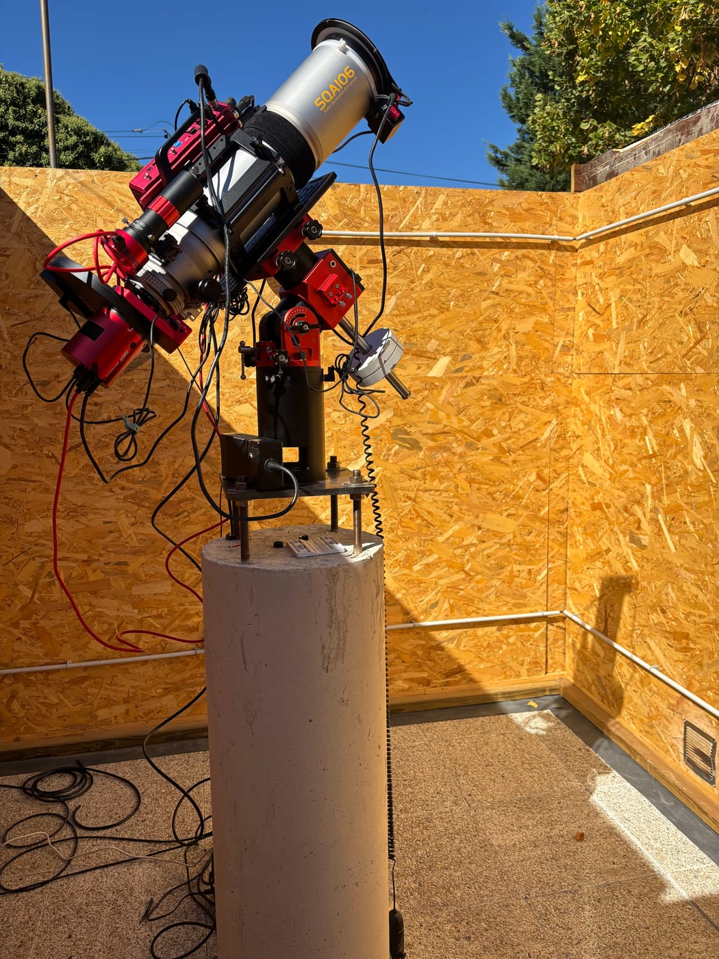 L’instrument sur son pilier cylindrique en béton, au centre de l’abri ouvert, les parois intérieures en panneaux de bois et le sol autour.